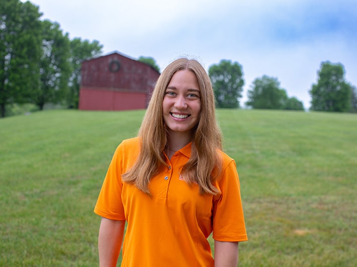 Headshot of Lara Woodley wearing a Herbert polo in a field with a red barn in the background.