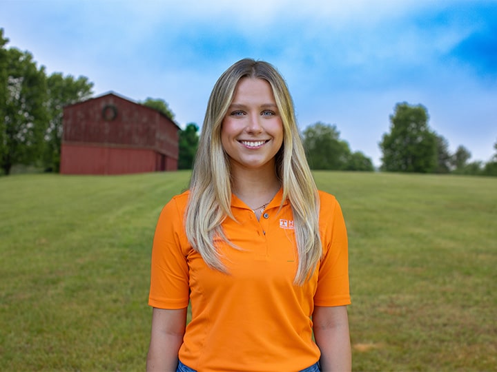 Headshot of Lexi Roth wearing a Herbert polo in a field with a red barn in the background.