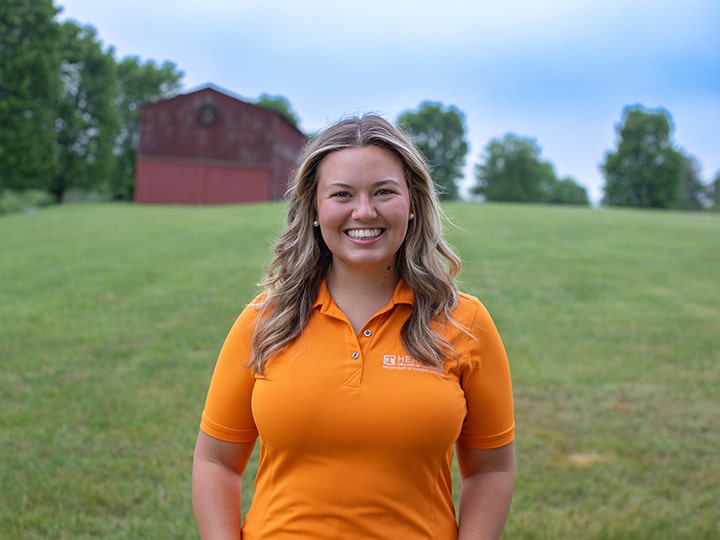 Headshot of Lucy Bacon wearing a Herbert polo in a field with a red barn in the background.