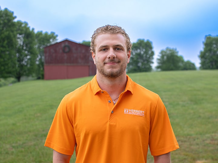 Headshot of Luke Davis wearing a Herbert polo in a field with a red barn in the background.
