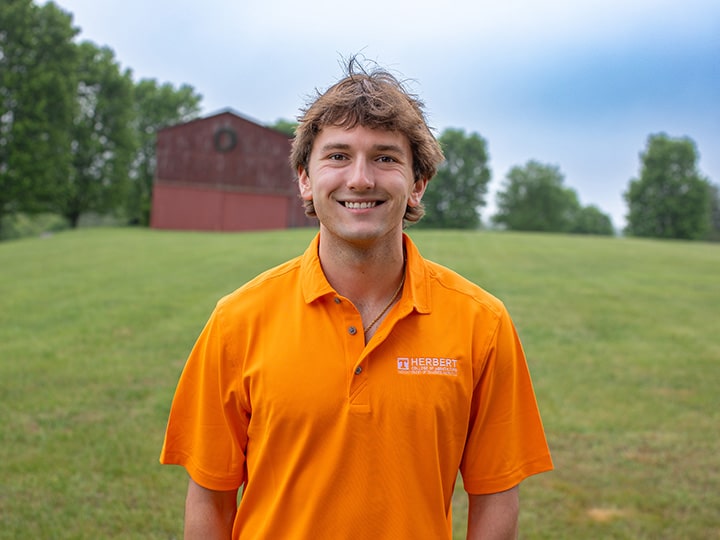 Headshot of Matthew Digby wearing a Herbert polo in a field with a red barn in the background.