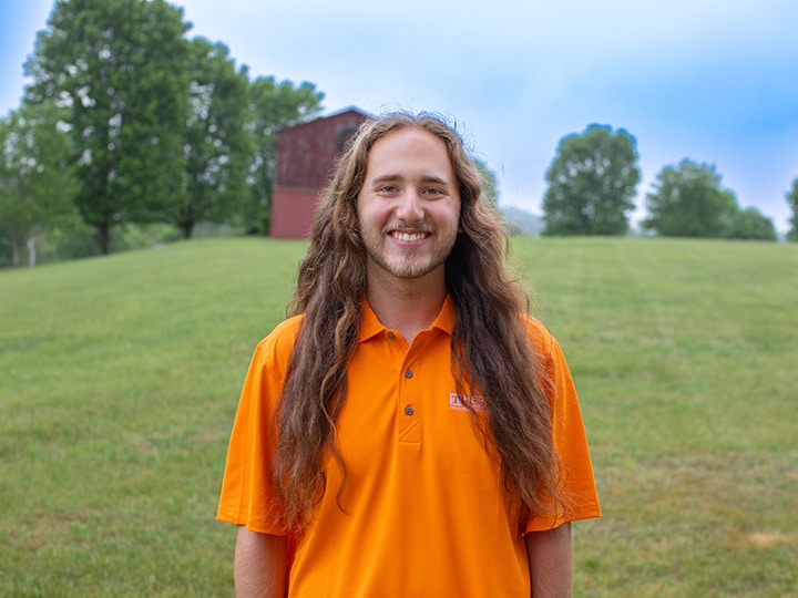Headshot of Matthew McKheen wearing a Herbert polo in a field with a red barn in the background.