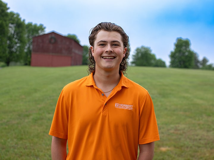 Headshot of Rhyder Short wearing a Herbert polo in a field with a red barn in the background.