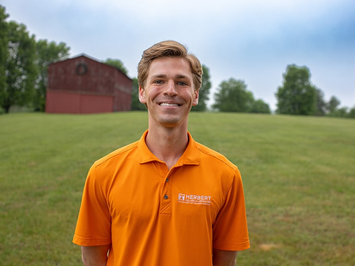 Headshot of Sloan Hoesel wearing a Herbert polo in a field with a red barn in the background.