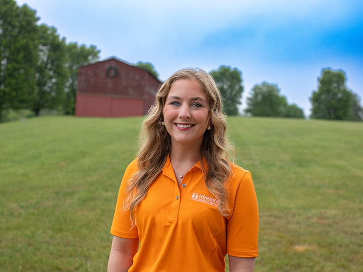 Headshot of Sophia Anderson wearing a Herbert polo in a field with a red barn in the background.