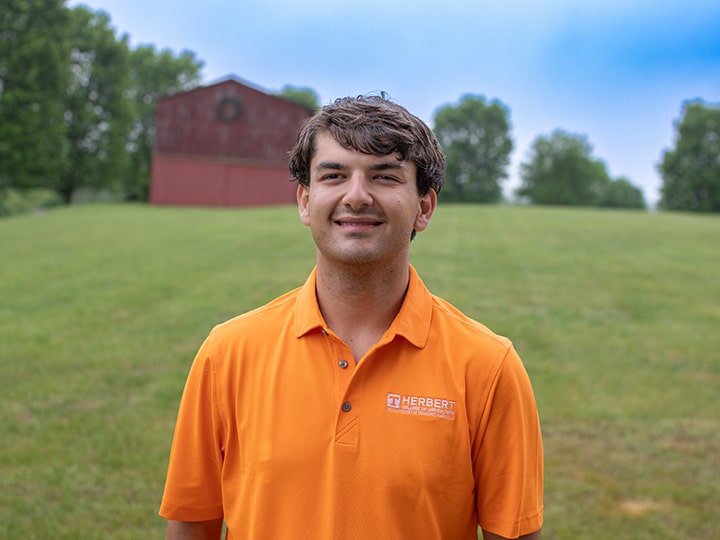 Headshot of Zachary Feldman wearing a Herbert polo in a field with a red barn in the background.