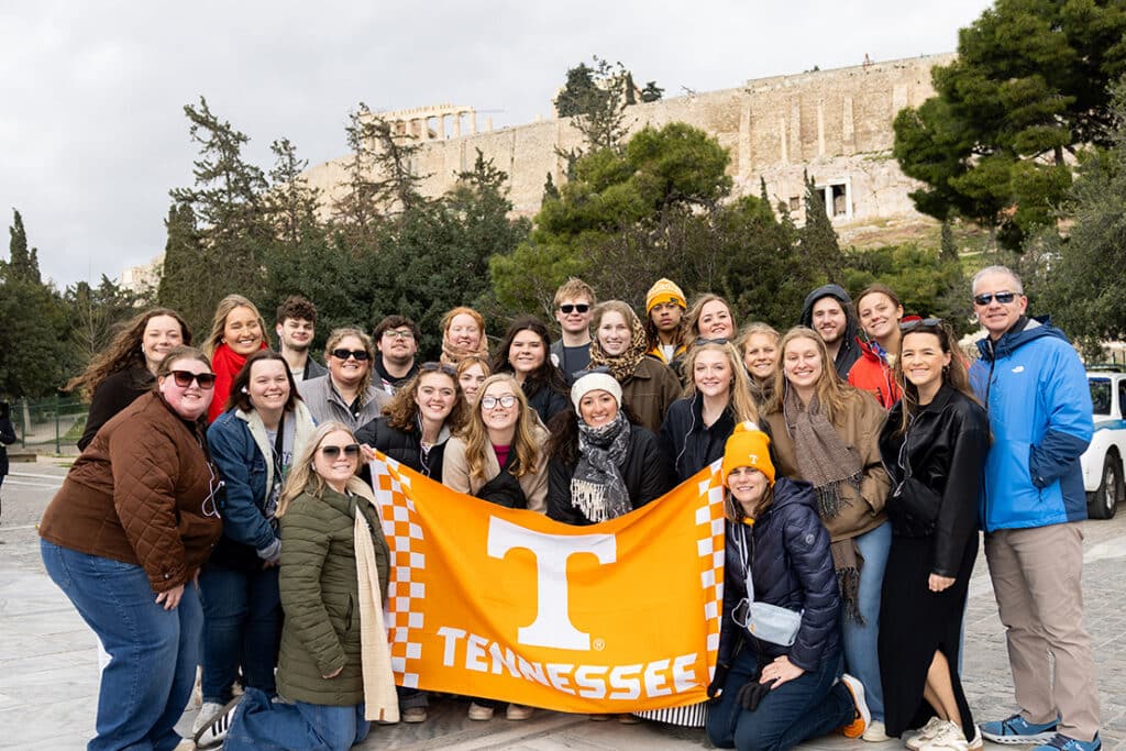 A group of students on a study abroad trip in Greece holding up a Tennessee flag.