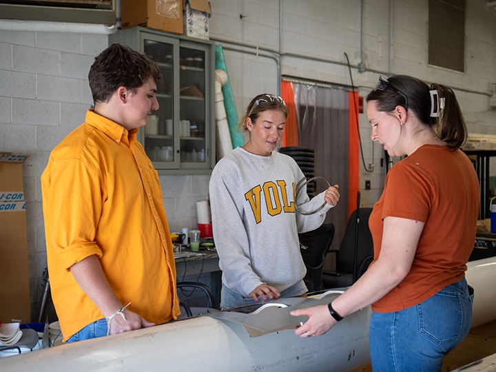 Three University of Tennessee students work together on a biosystems engineering project in a workshop, examining and measuring materials.