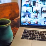 A coffee cup sits in front of an open laptop showing an online meeting.