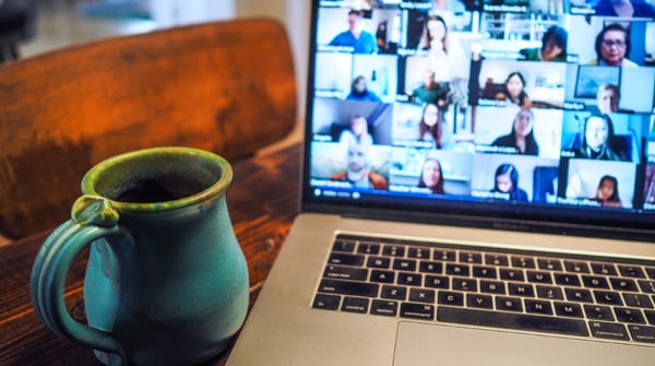A coffee cup sits in front of an open laptop showing an online meeting.
