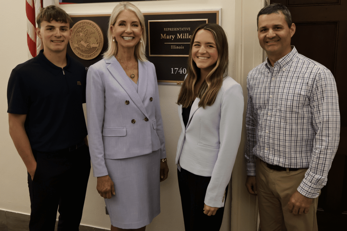 Four individuals posing and smiling in front of a sign that says "Representative Mary Miller, Illinois"