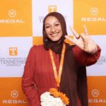 Junior environmental science student Jannat Bahanni at the 2025–26 Regal Scholars ceremony holding up the "Vols" sign with a Regal and UT banner behind her.