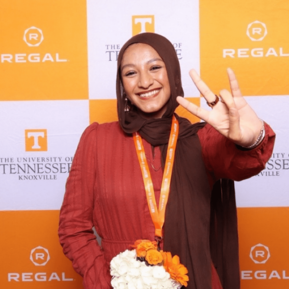 Junior environmental science student Jannat Bahanni at the 2025–26 Regal Scholars ceremony holding up the "Vols" sign with a Regal and UT banner behind her.