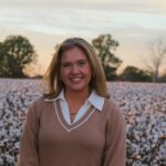 Callie Robinson wearing a tan sweater over a white collar shirt in a flower field.