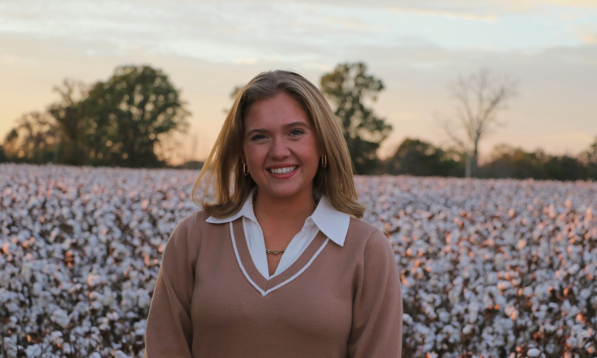Callie Robinson wearing a tan sweater over a white collar shirt in a flower field.